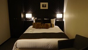 Habitación de hotel con una cama grande, dos mesitas de noche con lámparas, un cuadro enmarcado en la pared y un cabecero de color oscuro.