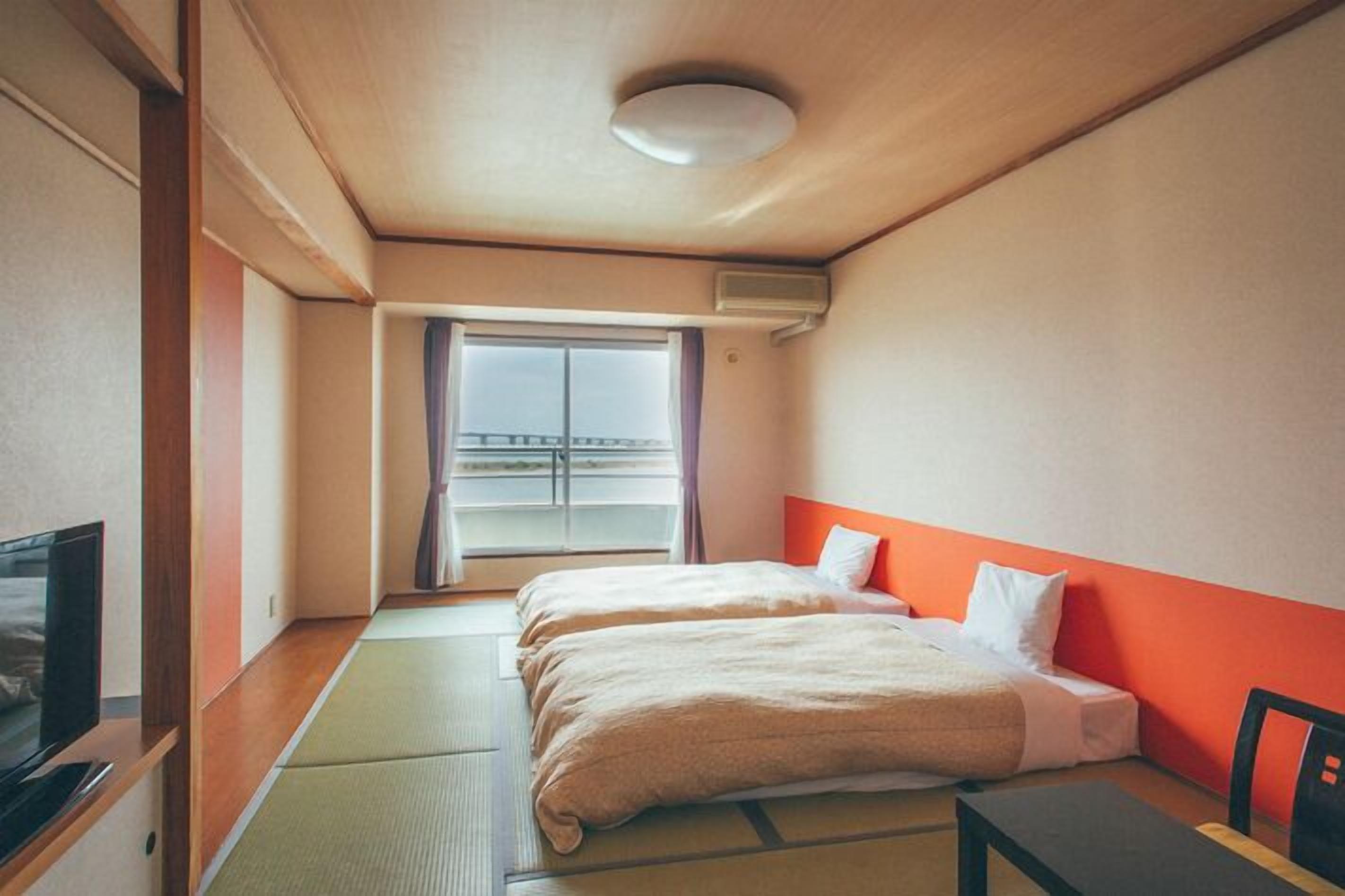A hotel room with two beds, a TV, a small table, and a window with a view.
