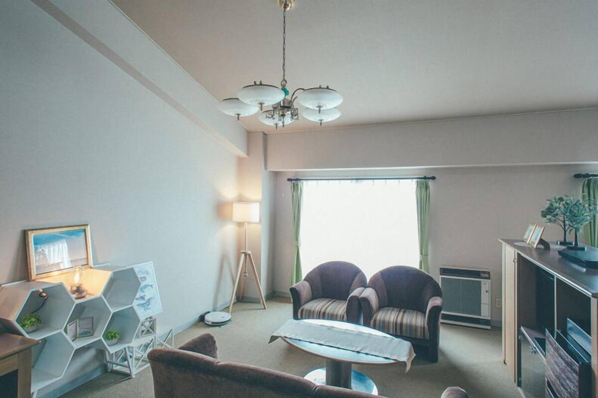 Ein Wohnzimmer mit einer Couch, einem Couchtisch, einer Lampe, einem sechseckigen Stauraum und einem großen Fenster mit Vorhängen.