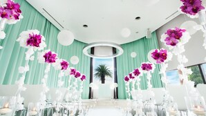 A wedding venue with a central aisle decorated with white and purple flowers, a view of palm trees, and a modern ceiling design. - Hamanako Resort & Spa The Ocean (Hamamatsu)