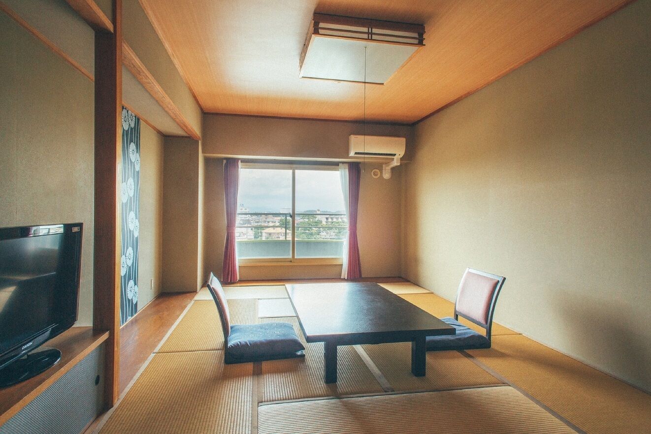 A room with tatami flooring, a television, a table, and a chair.
