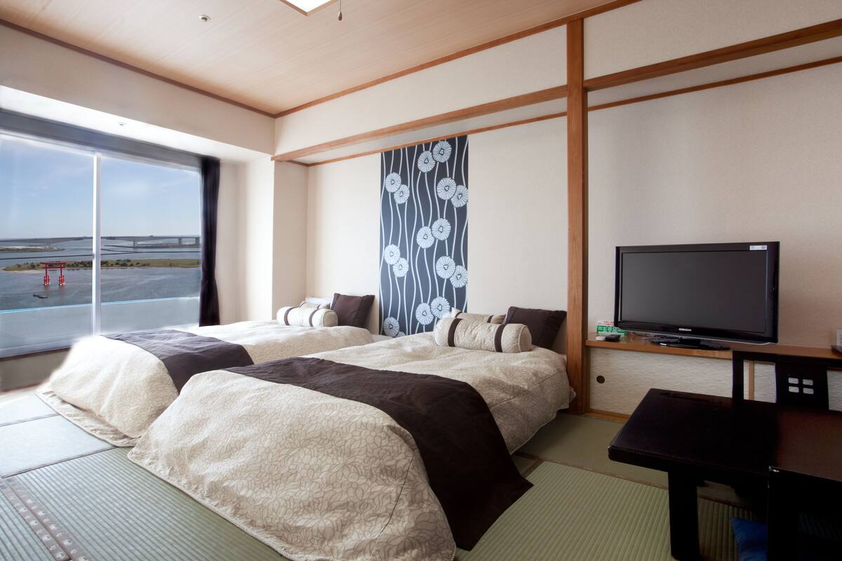 Ein Hotelzimmer mit zwei Betten, einem Fernseher und Blick auf eine Brücke und Wasser.