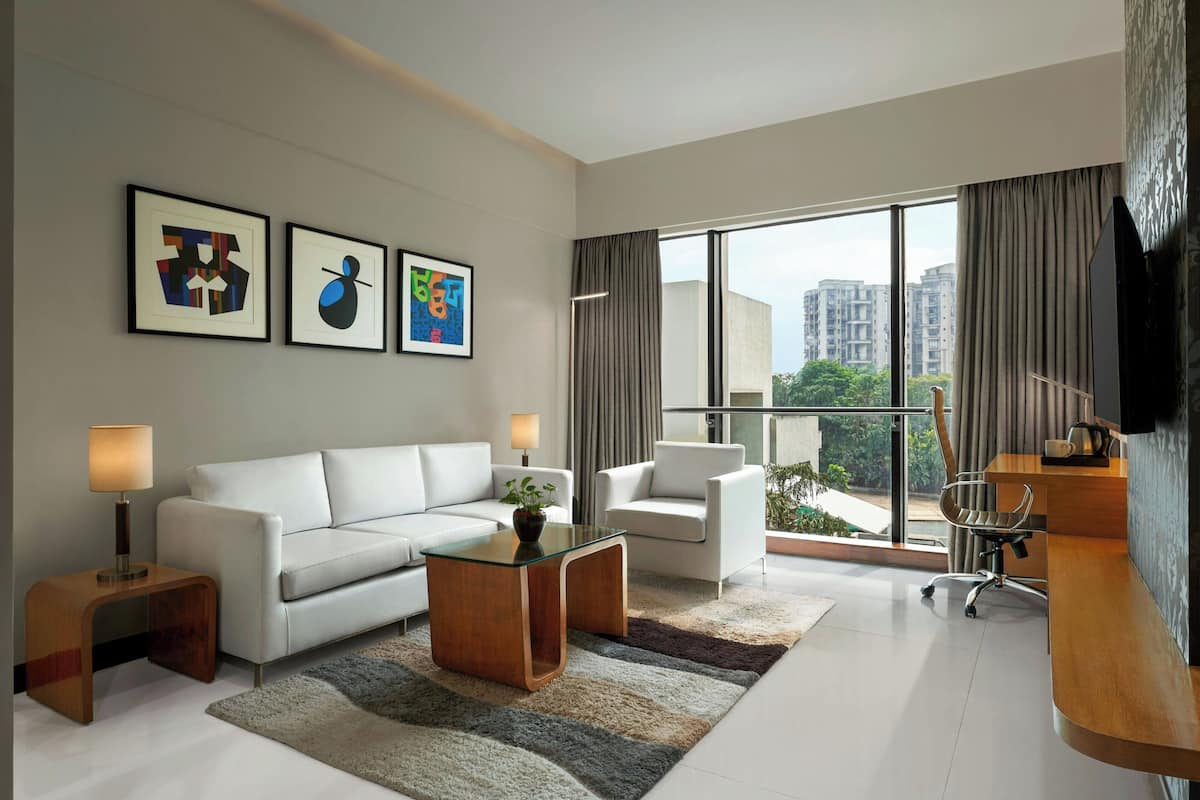 A modern living room with a white sofa, a glass coffee table, a wooden side table, a chair, and a TV on a wooden stand.