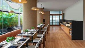 A modern restaurant with long communal tables, wicker pendant lighting, and a view of lush greenery through large windows. - The Fern Residency Mumbai, The Acres Chembur, Series by Marriott (Mumbai)
