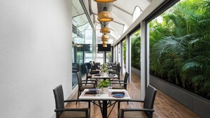 A restaurant with a long table, wicker chairs, and a view of lush greenery. - The Fern Residency Mumbai, The Acres Chembur, Series by Marriott (Mumbai)