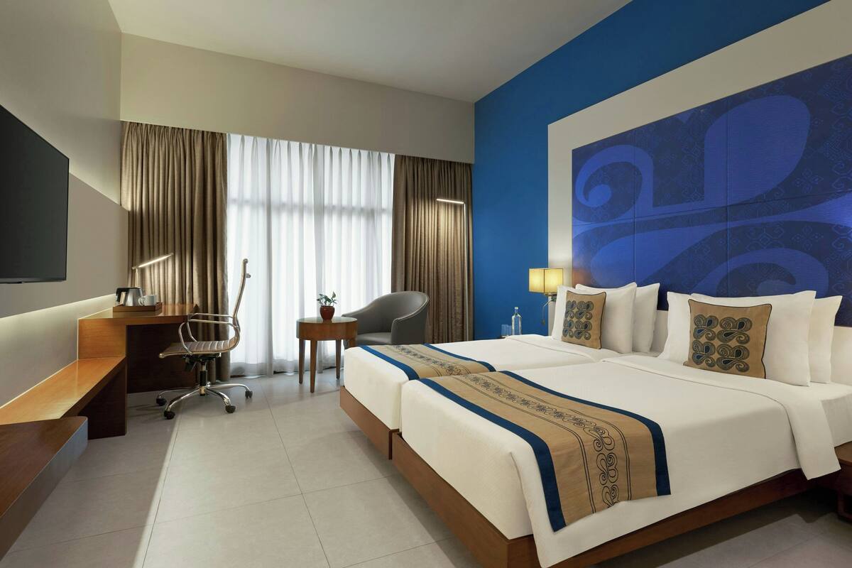 A hotel room with a bed, desk, chair, and a large wall decoration.