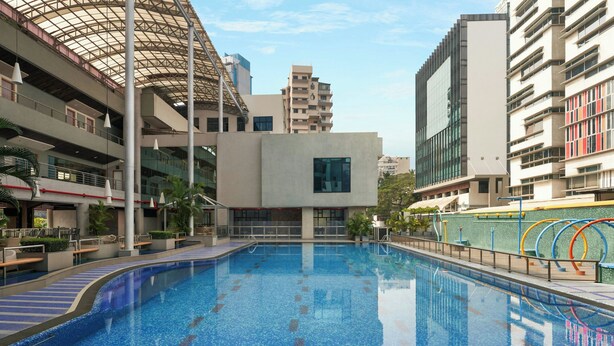 A swimming pool with a modern architectural setting, including a glass facade building and a multi-story structure with balconies. - The Fern Residency Mumbai, The Acres Chembur, Series by Marriott (Mumbai)