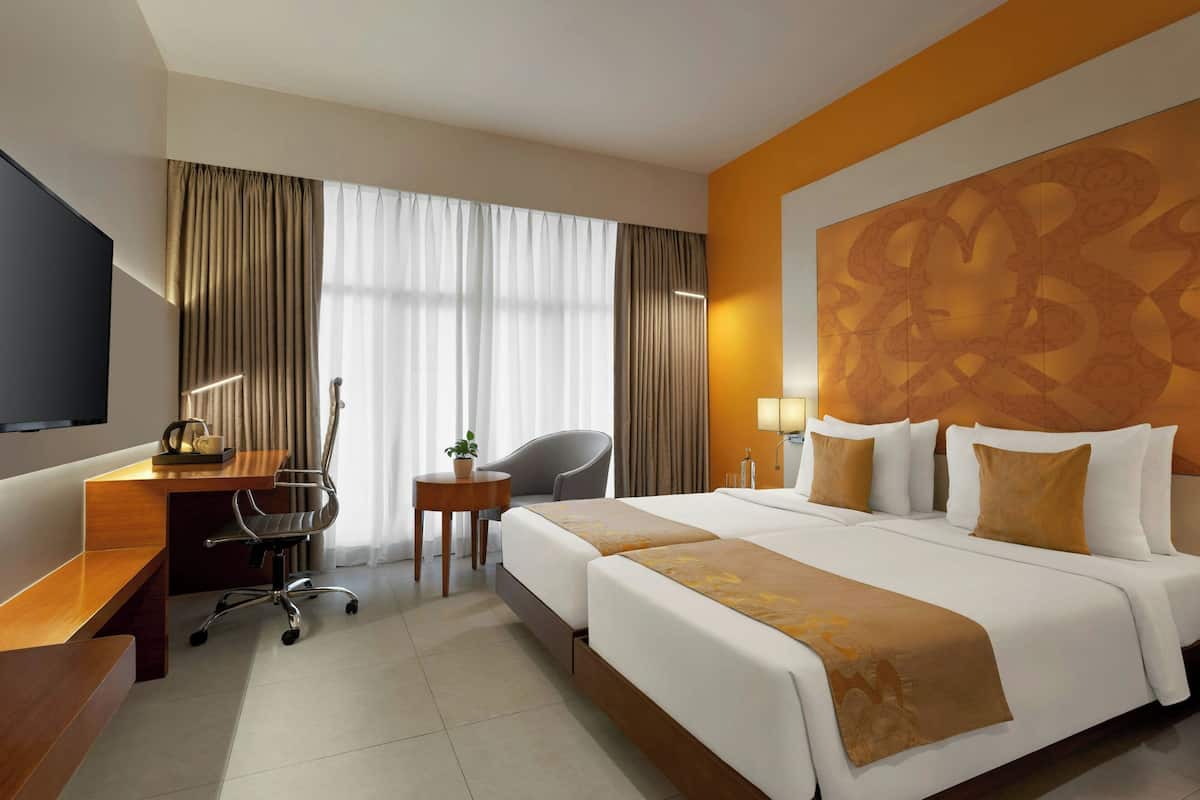 A hotel room with a bed, a desk, a chair, a TV, and a large wall decoration.