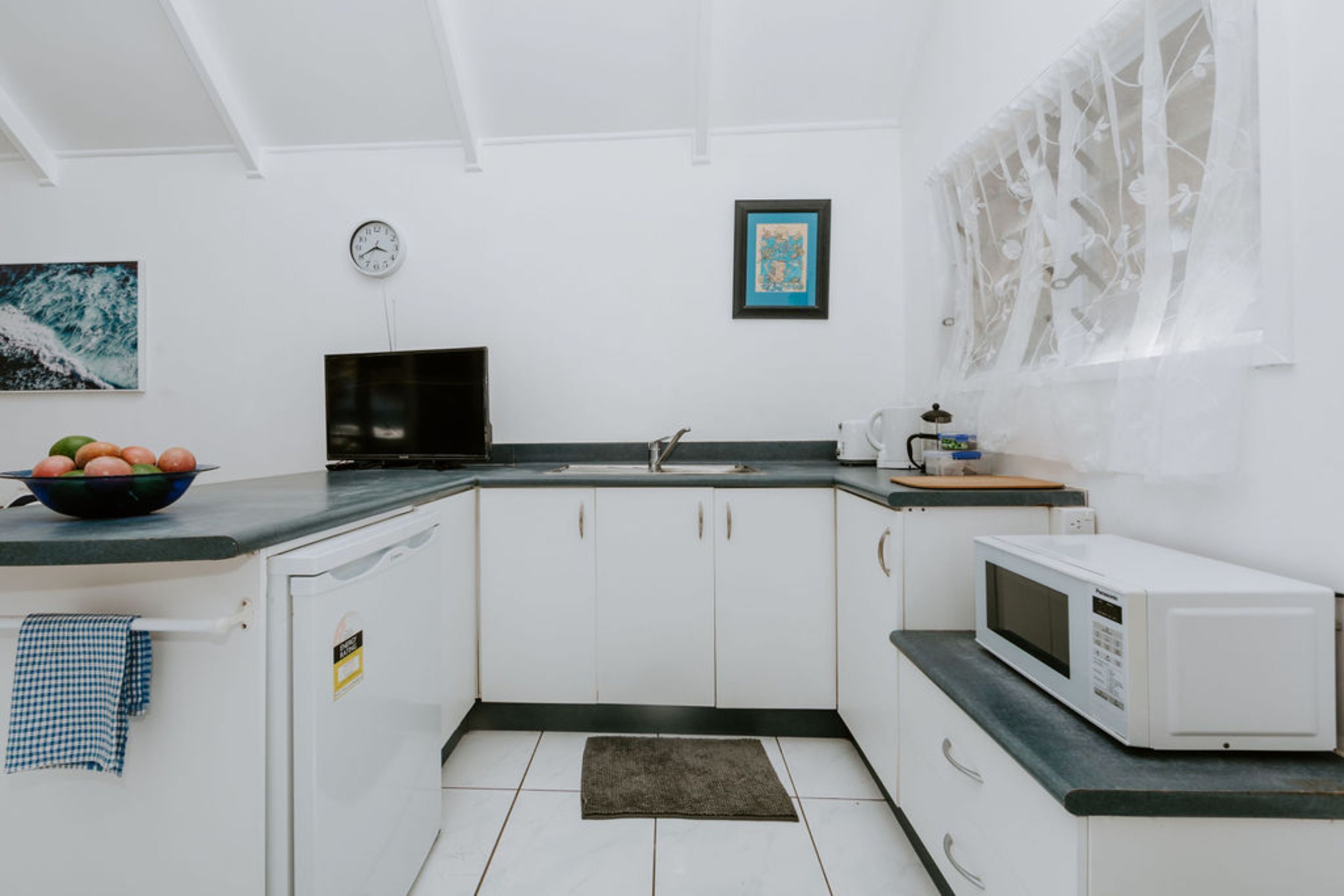 Une cuisine moderne avec des meubles blancs, un plan de travail noir, un four à micro-ondes, un évier et une horloge au mur.