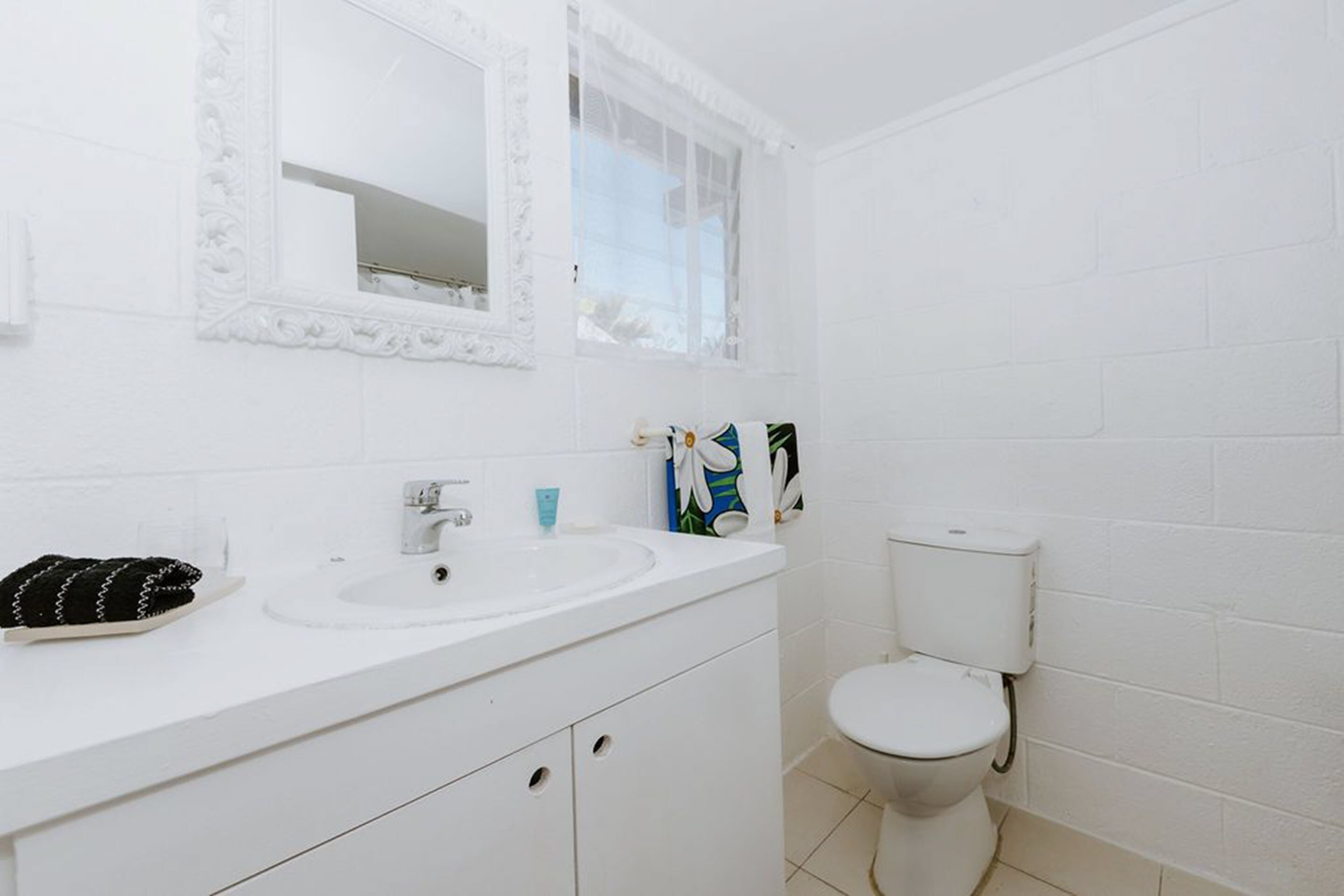 A white bathroom with a sink, mirror, and toilet.