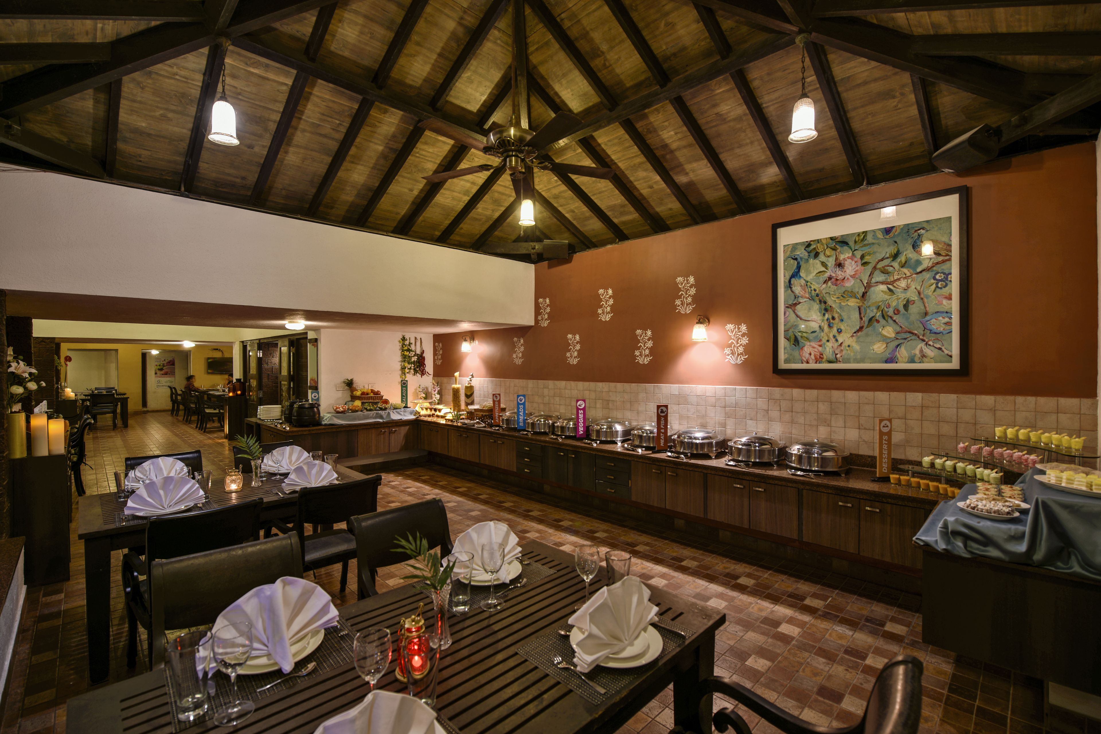 Een restaurant met houten tafels gedekt voor een maaltijd, een buffet en een groot bloemschilderij aan de muur.