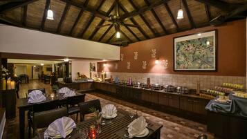 Een restaurant met houten tafels gedekt voor een maaltijd, een buffet en een groot bloemschilderij aan de muur.
