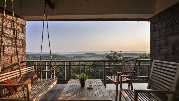 A wooden deck with a swing chair, a table with a potted plant, and a view of a mountainous landscape. - The Fern Samali Resort Dapoli, Series by Marriott (Dapoli)
