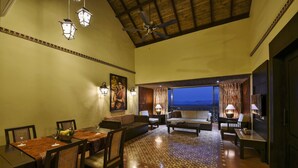 A spacious living area with a high ceiling, a dining table set with chairs, a sofa, and a coffee table. There are wall-mounted lamps and a view of the outside through a large window. - The Fern Samali Resort Dapoli, Series by Marriott (Dapoli)