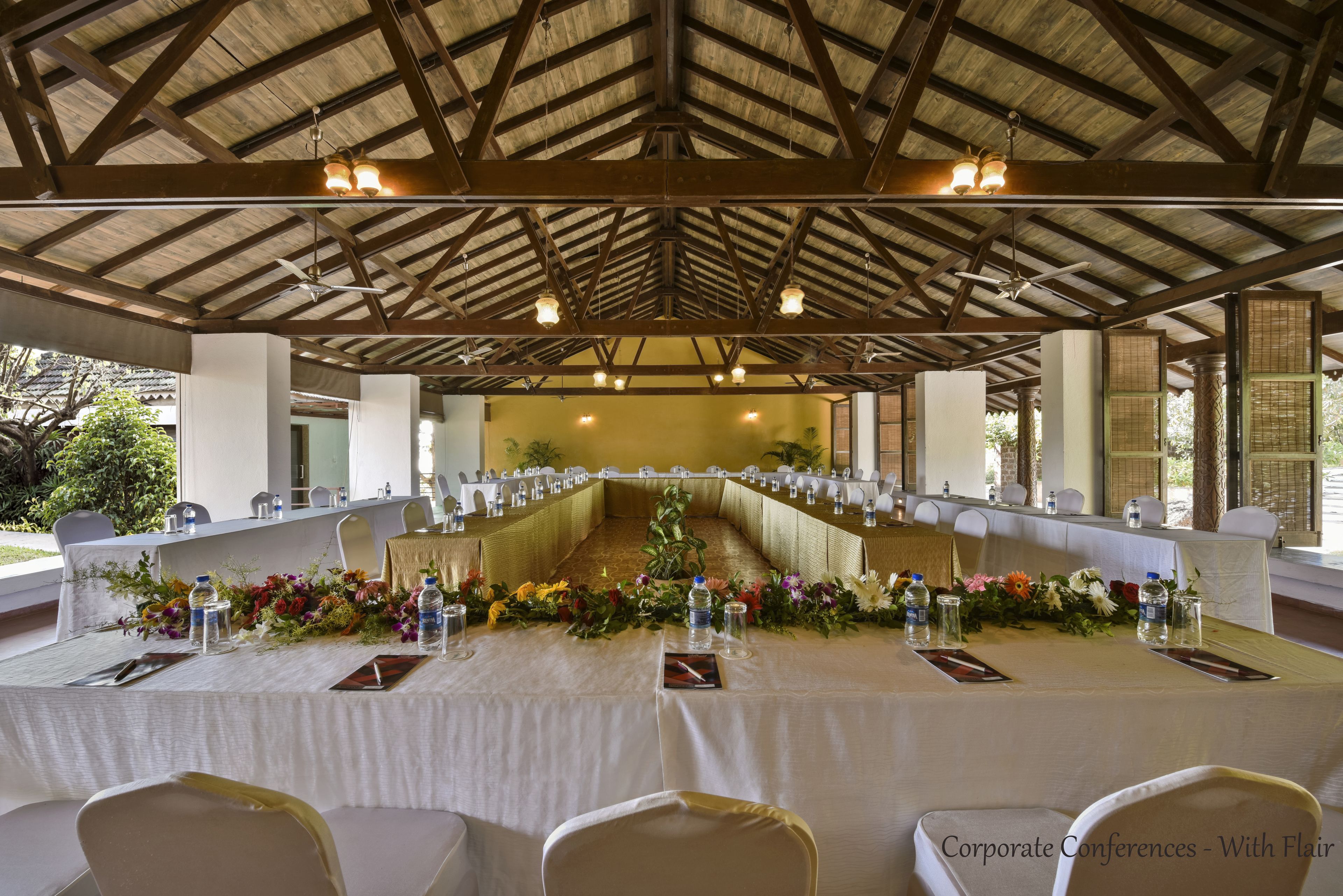 Una sala de conferencias con una mesa larga, sillas blancas y centros de mesa con flores.