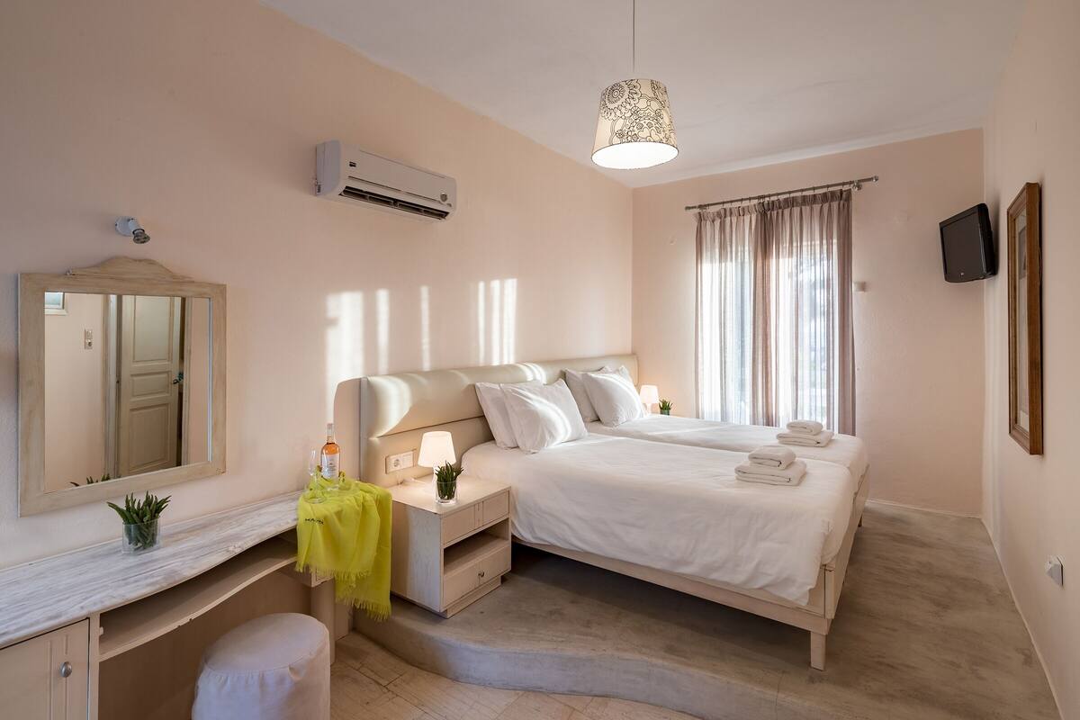 A bedroom with a bed, bedside tables, a mirror, an air conditioning unit, a television, and a window with curtains.