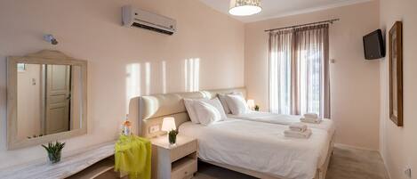 Une chambre à coucher comprenant un lit, des tables de chevet, un miroir, un appareil de climatisation, un téléviseur et une fenêtre avec des rideaux.