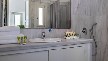 Un baño con lavamanos blanco, un espejo, ducha y toallero.