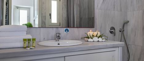 Un baño con lavamanos blanco, un espejo, ducha y toallero.