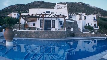 Um hotel com piscina, área de estar ao ar livre e montanhas ao fundo.