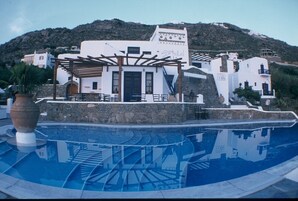 Um hotel com piscina, área de estar ao ar livre e montanhas ao fundo.