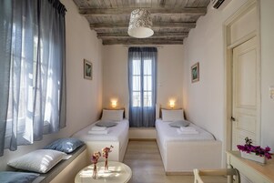 A room with two beds, a small table with flowers, a window with curtains, and a door.