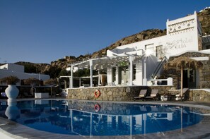 A pool area with lounge chairs, a stone wall, and a building labeled "Hotel OLIYA". - Olia Hotel (Mykonos)