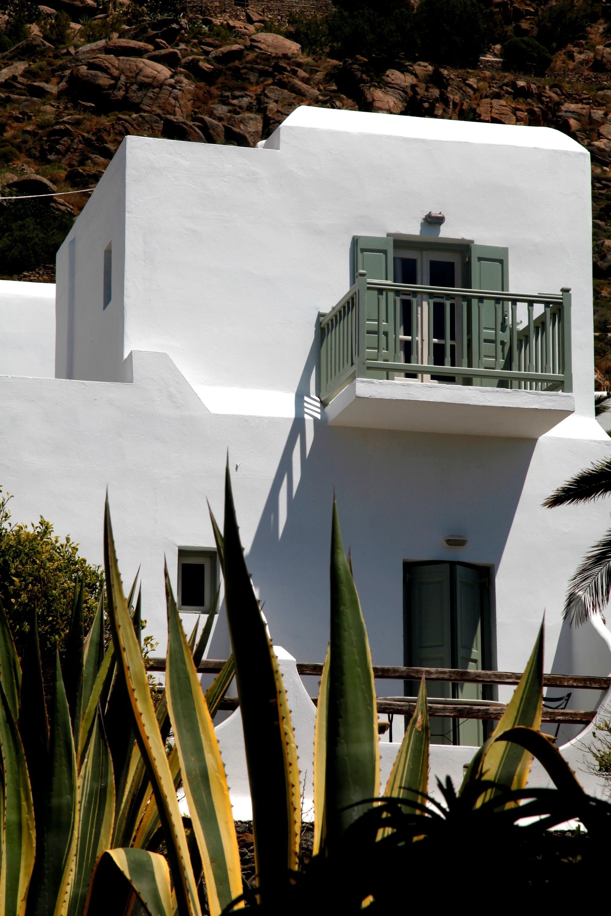 A white building with a balcony, surrounded by plants.