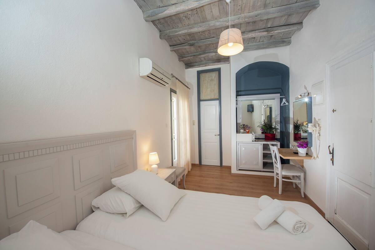 A bedroom with a bed, bedside table, lamp, and a desk with a chair.
