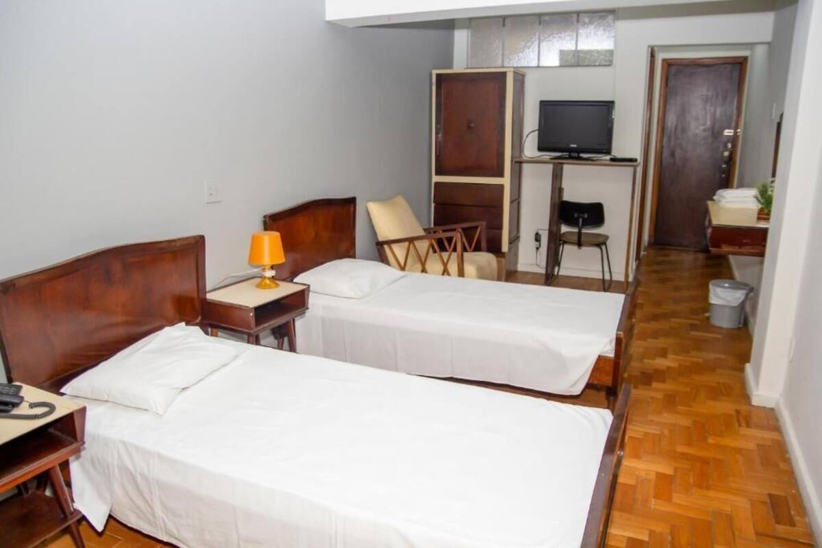 A hotel room with two single beds, a desk with a telephone, a chair, a TV, and a wardrobe.
