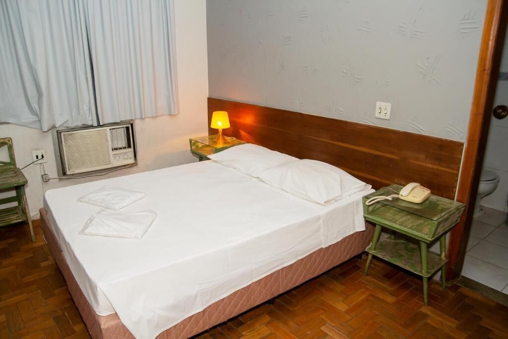 Ein Hotelzimmer mit Bett, Nachttischlampe, Telefon und Heizkörper.