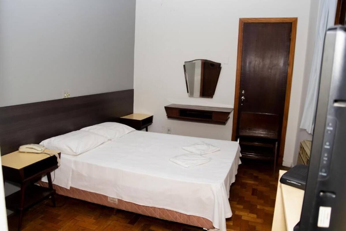 A hotel room with a bed, bedside table, and a desk with a telephone.