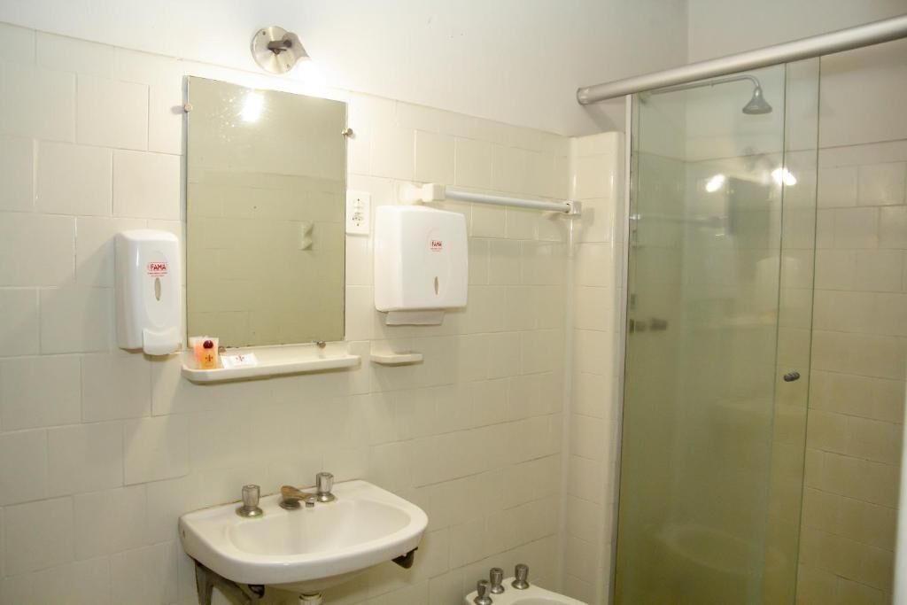 Un baño con lavamanos, espejo, dispensador de jabón y cabina de ducha de vidrio.
