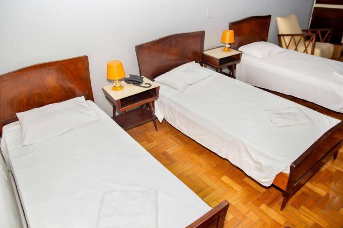 A hotel room with two single beds, wooden headboards, and bedside tables with lamps.