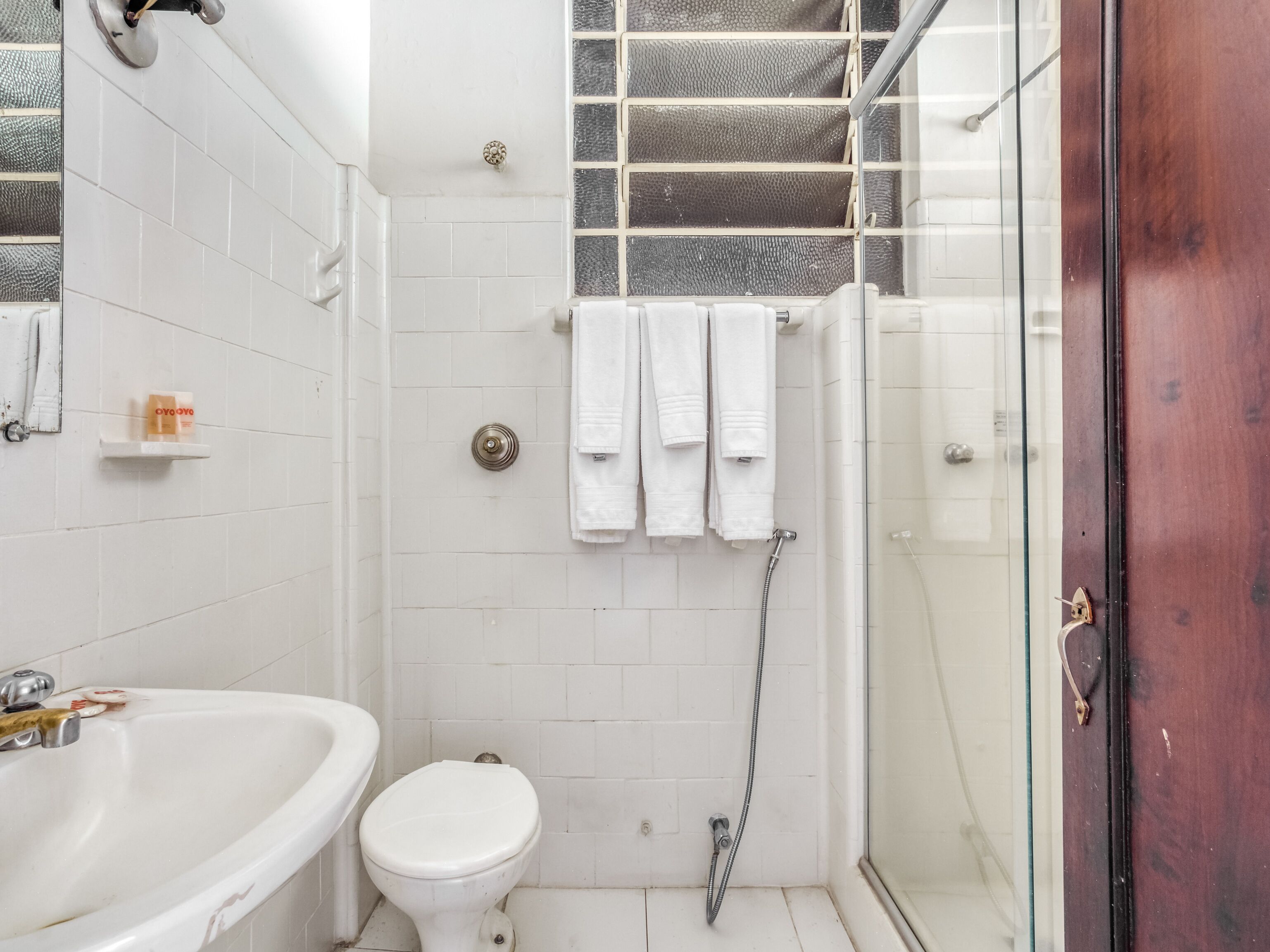A bathroom with a white sink, toilet, and shower. There are three white towels hanging on a rack.