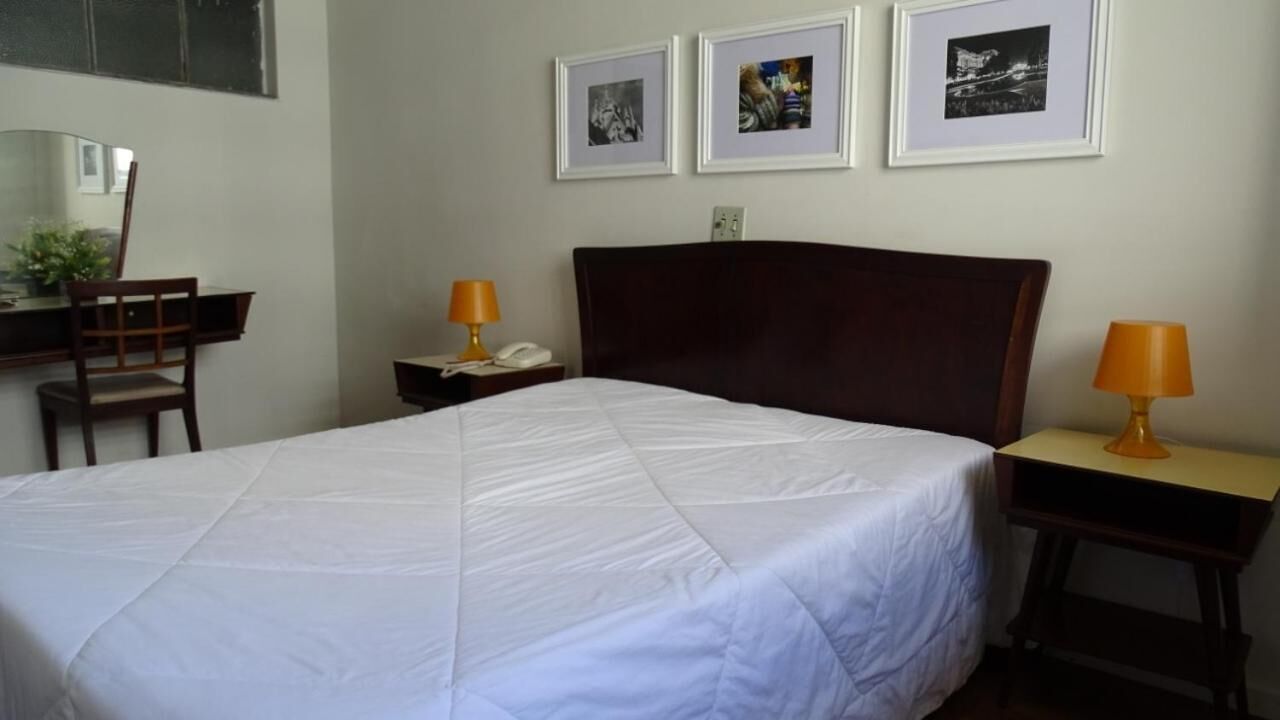 A hotel room with a large bed, a desk with a chair, two bedside lamps, and three framed pictures on the wall.