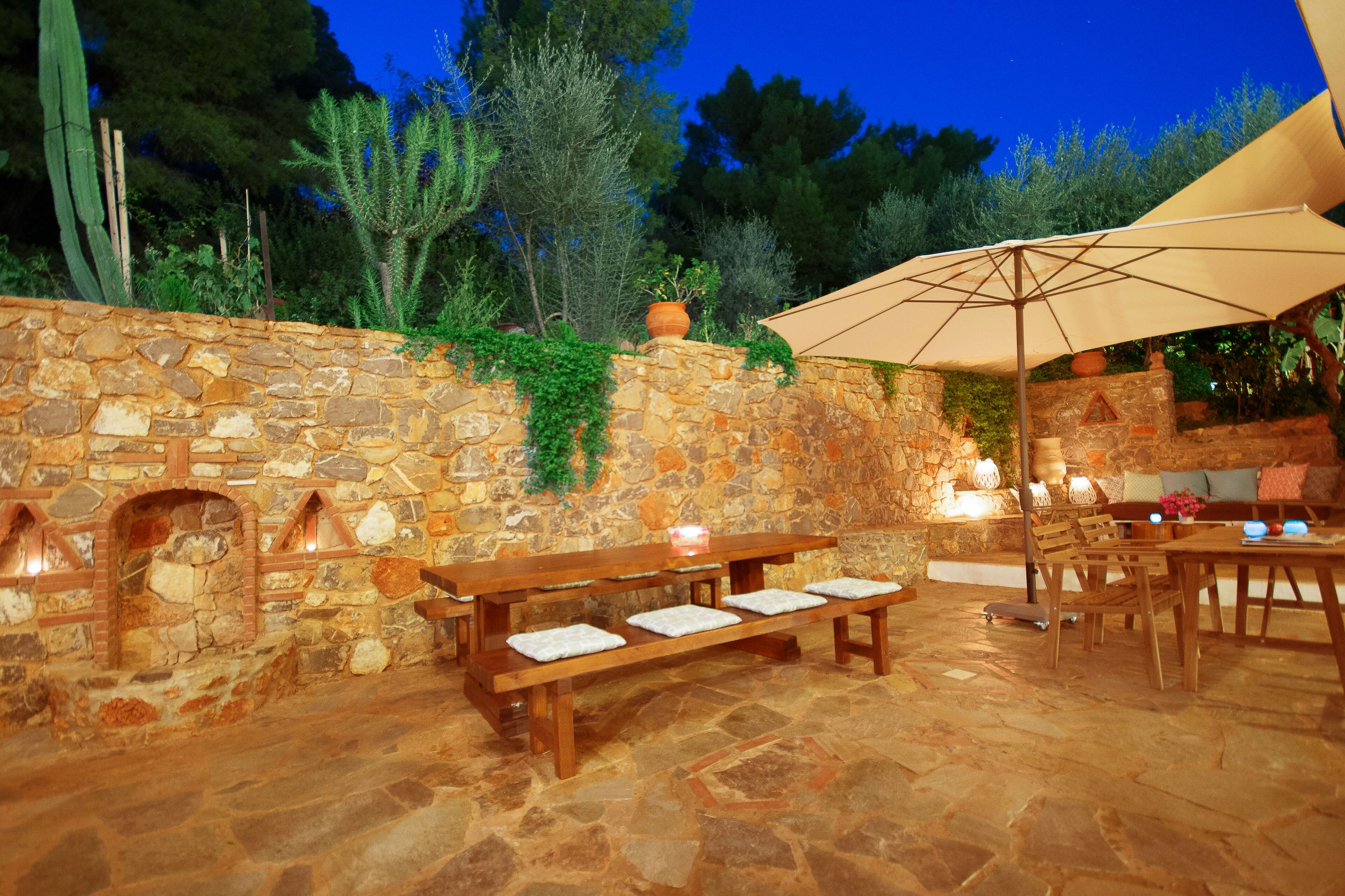 An outdoor patio with stone walls, wooden benches, and a table with chairs.