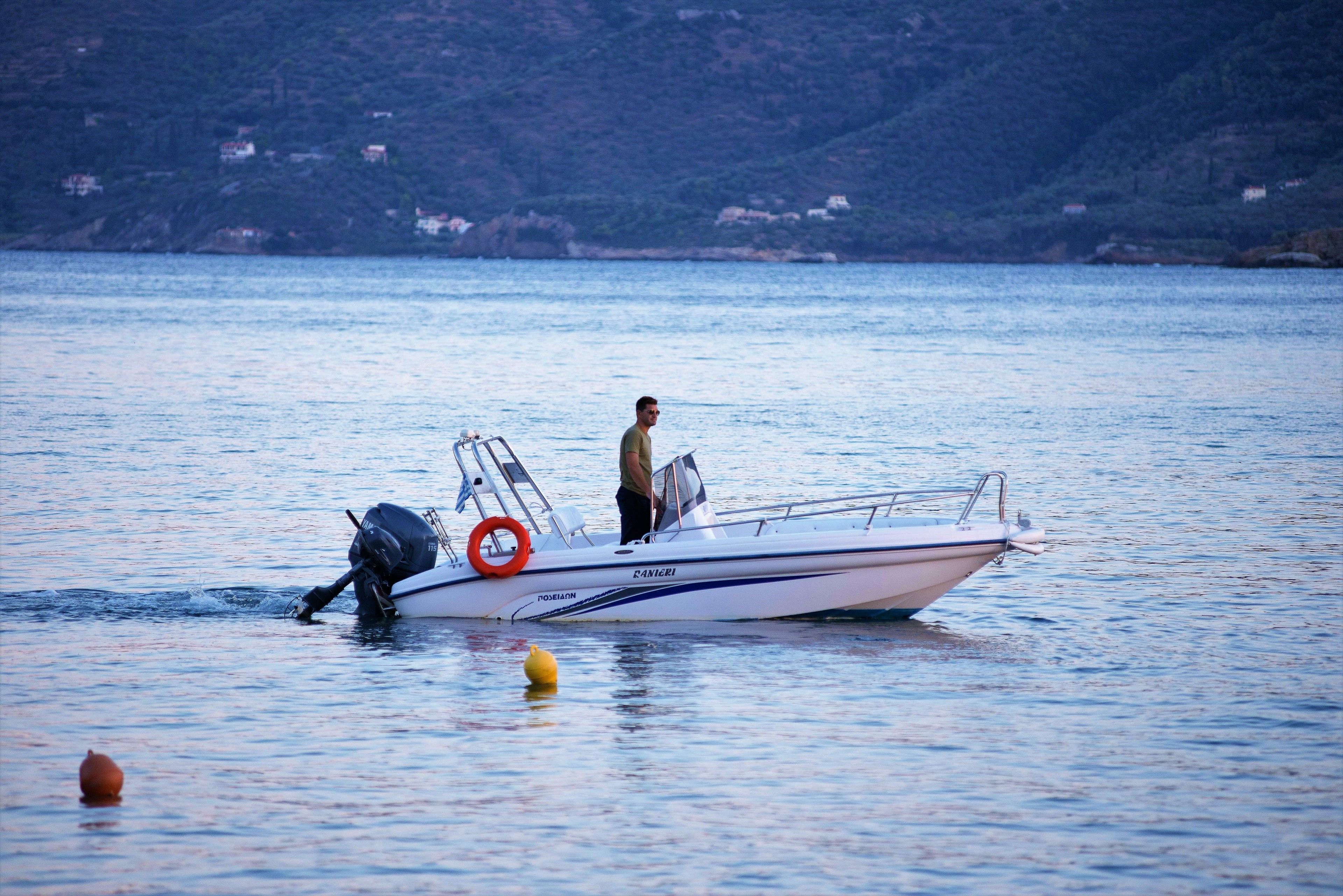 A small motorboat with a person standing on the deck, a life preserver, and buoys in the water.