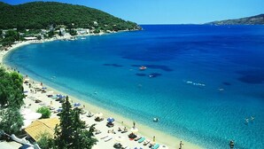 Una spiaggia costiera con acque blu cristalline, una riva sabbiosa e colline verdi sullo sfondo.