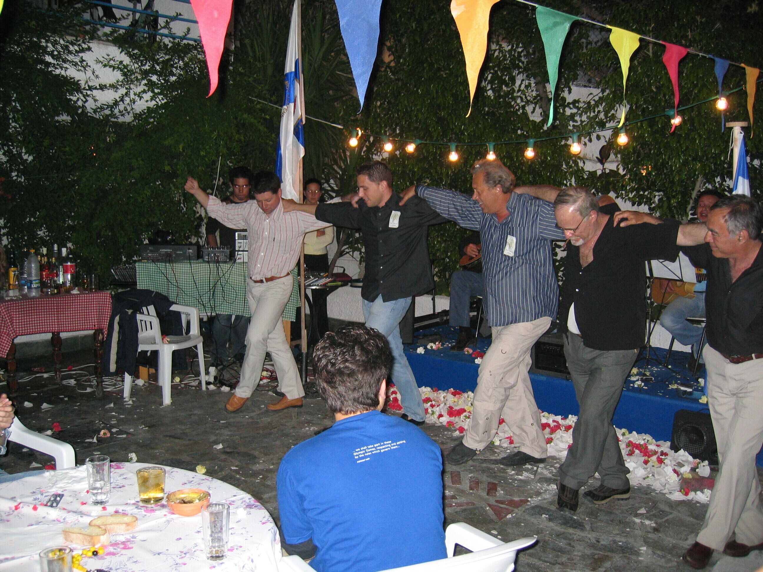 Un gruppo di persone che ballano durante un evento all'aperto, con tavoli e sedie disposti intorno.