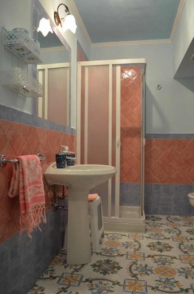 Un baño con lavamanos pedestal, toallero con toalla, cabina de ducha y baldosas de suelo estampadas.
