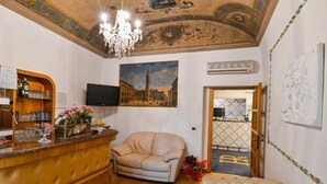 A living room with a wooden bar, a beige sofa, a television, and a painting of a cityscape. - Hotel PRime già Hotel Piccolo Ritz (Pistoia)