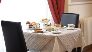 A breakfast table set with bread, fruit, and coffee, with a view of a radiator and curtains in the background. - Hotel PRime già Hotel Piccolo Ritz (Pistoia)