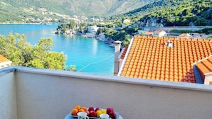 Een balkon met een tafel, bedekt met fruit en twee stoelen, met uitzicht op een meer en bergen.