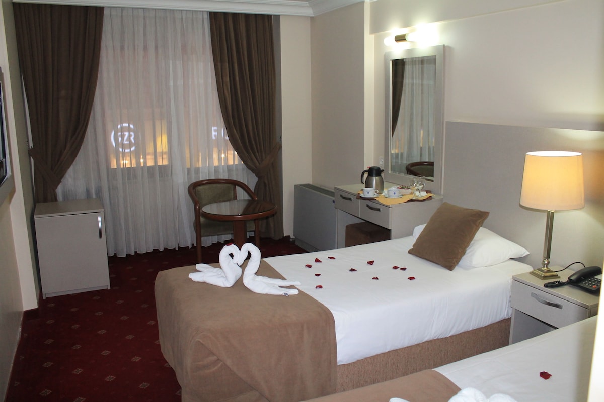 A hotel room with two beds, a desk, a chair, a small refrigerator, a lamp, and a telephone.