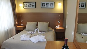 Une chambre d’hôtel avec un lit bien fait, une tête de lit en bois, des lampes de chevet et une bouteille de vin posée sur la table de chevet.
