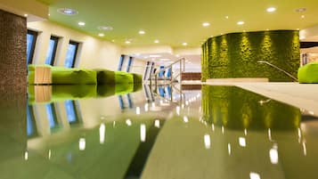A modern indoor pool area with a reflective floor, green seating, and a green textured wall.