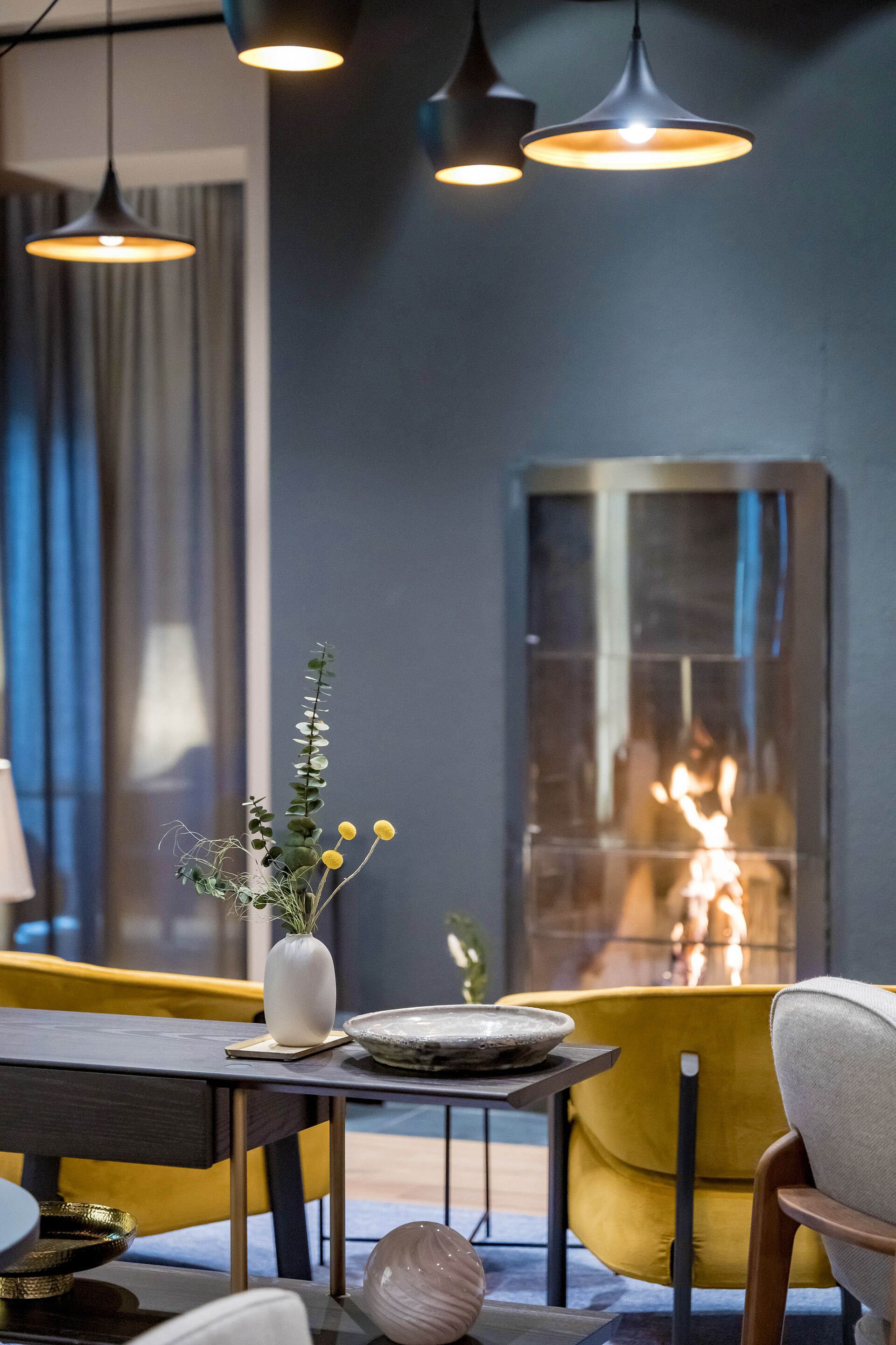 Een moderne woonkamer met een open haard, een eettafel en geel-grijs meubilair.