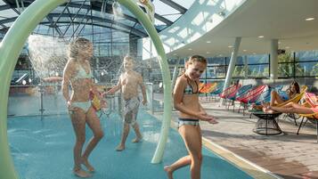 Ein moderner, überdachter Poolbereich mit einer Wasserspielanlage und Liegestühlen.