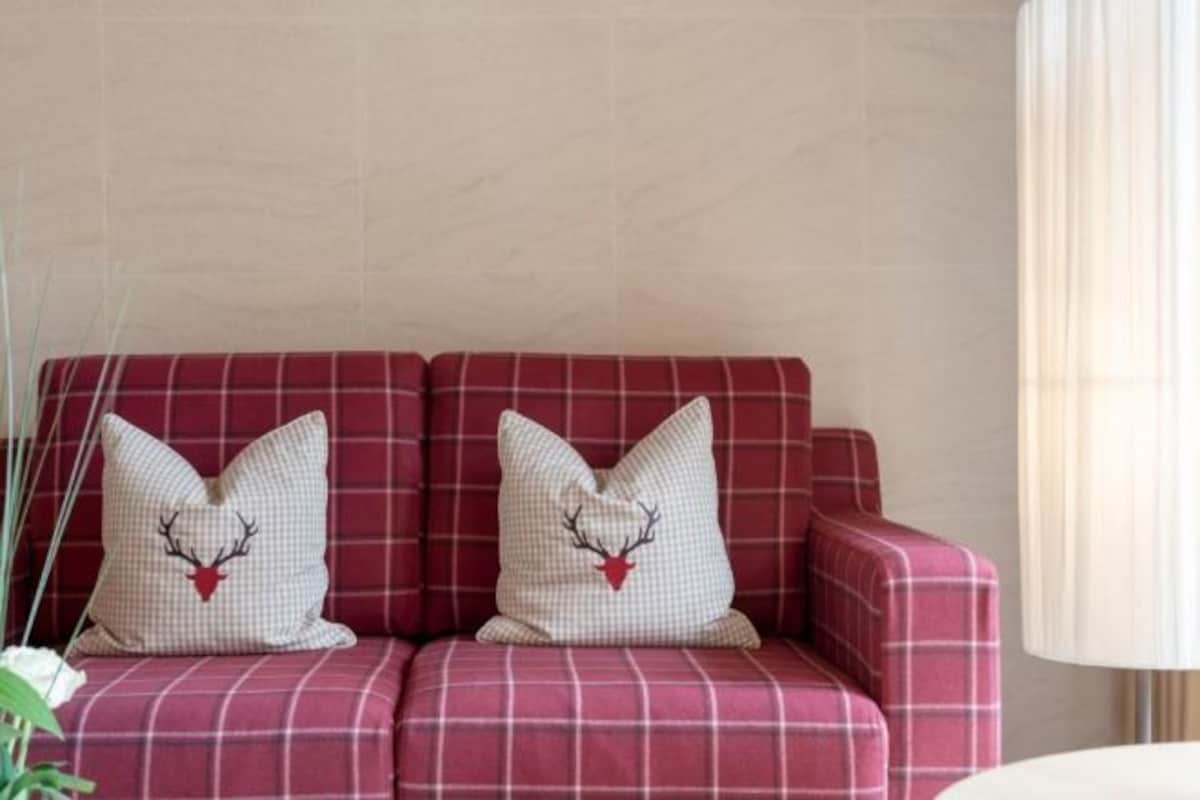 Un sofá rojo de cuadros con dos almohadones decorativos que muestran un diseño de cabeza de ciervo.